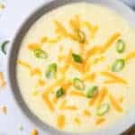 Top view photo of 4 Ingredient Potato Soup in a white bowl topped with shredded cheddar cheese and sliced green onions.