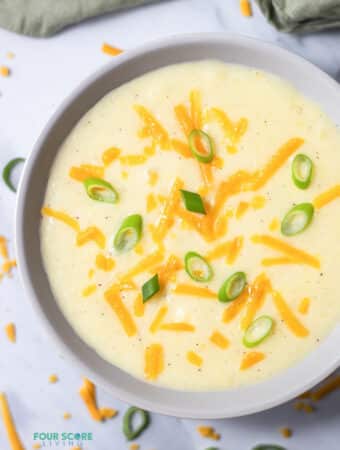 Top view photo of 4 Ingredient Potato Soup in a white bowl topped with shredded cheddar cheese and sliced green onions.