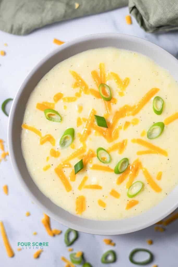 Top view photo of 4 Ingredient Potato Soup in a white bowl topped with shredded cheddar cheese and sliced green onions. 