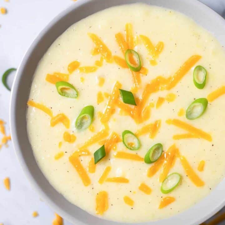 Top view photo of 4 Ingredient Potato Soup in a white bowl topped with shredded cheddar cheese and sliced green onions.