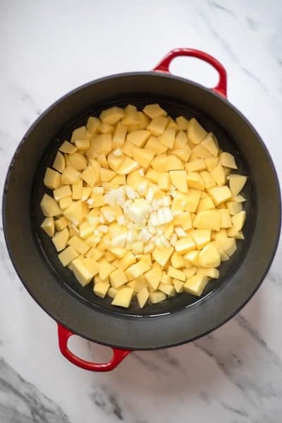 Top view photo of prepared potatoes and onions in a large stock pot.