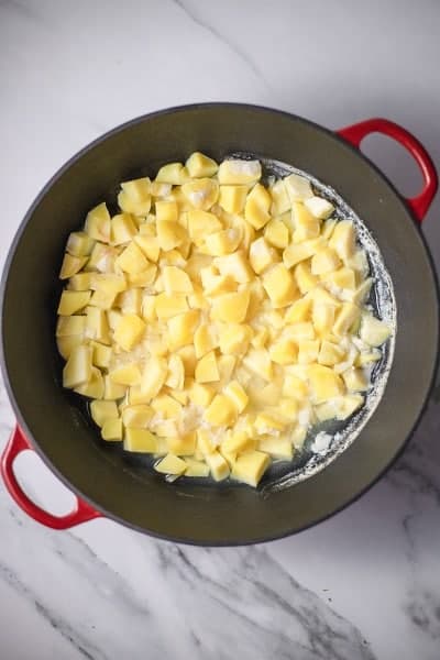 Top view photo of potatoes and onions covered in cold water, in a large stockpot.