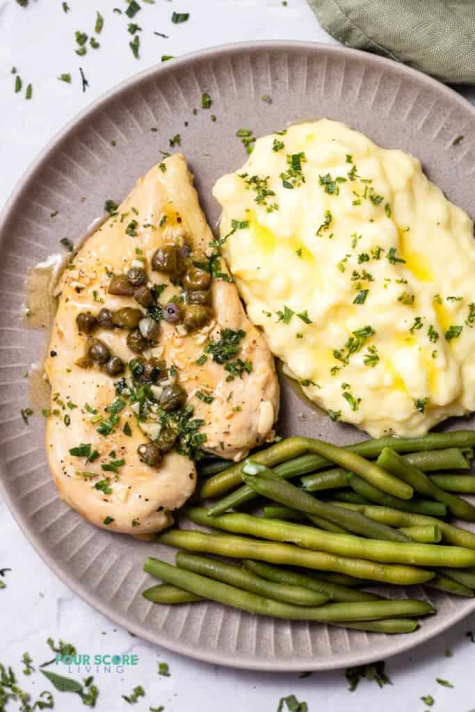 Top view photo of Chicken Paillard, on a plate with green beans and mashed potatoes. 