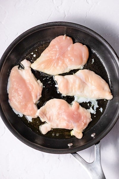 Top view photo of chicken cutlets in a frying pan, and cooking on one side until browned.