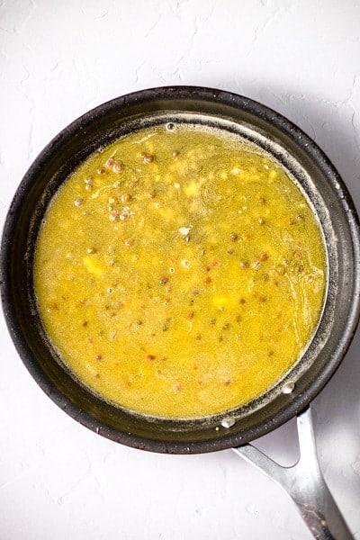Top view photo of a frying pan with garlic, butter, capers, and salt and pepper, mixed together.