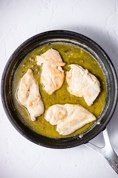 Top view photo of a frying pan with chicken cutlets and butter sauce.