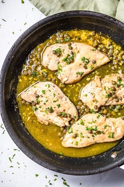 Top view photo of chicken in a frying pan with butter sauce, and cooked until chicken is cooked through.