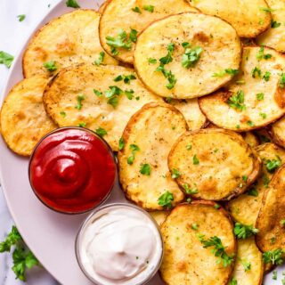 Top view photo of Cottage Fries on a white plate, with 2 sides of dipping sauces. The fries are garnished with chopped fresh parsley.