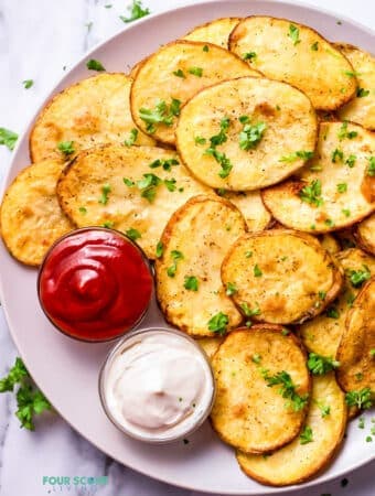 Top view photo of Cottage Fries on a white plate, with 2 sides of dipping sauces. The fries are garnished with chopped fresh parsley.