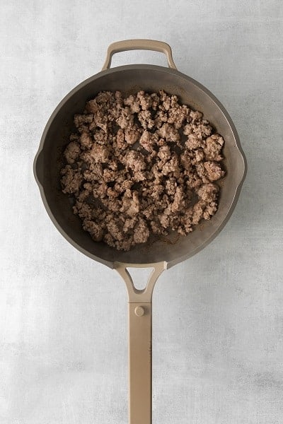 Top view photo of a skillet filled with ground pork that is cooked until brown.