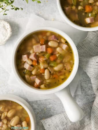 Top view photo of 3 bowls of Ham and White Bean Soup, ready to eat. There is a striped kitchen towel by the bowls.