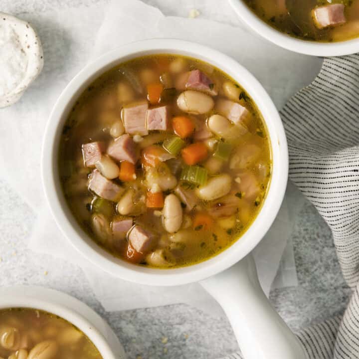 Top view photo of 3 bowls of Ham and White Bean Soup, ready to eat. There is a striped kitchen towel by the bowls.