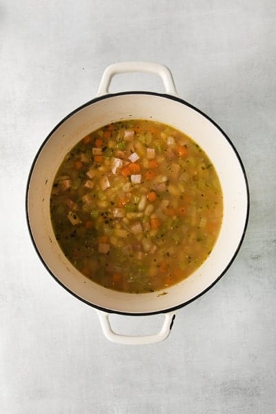 Top view photo of a large stockpot with all the ingredients to make Ham and White Bean Soup, simmering until warmed through.