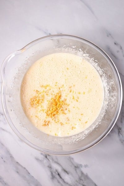 Top view photo of a clear bowl with orange juice and orange zest added in, ready to mix together.