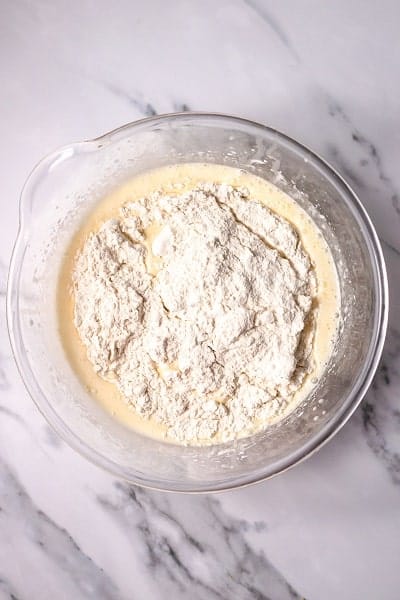 Top view photo of a clear bowl with the dry ingredients added to the wet ingredients in Italian Hangover Cake, ready to mix together.
