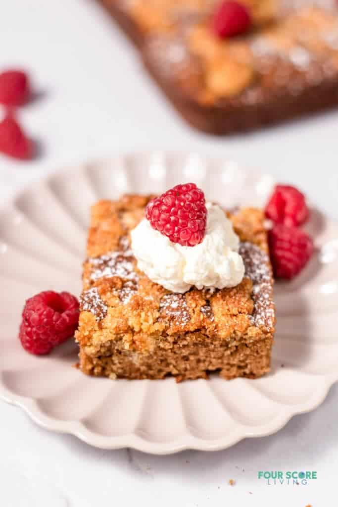 close up of a slice of keto coffee cake topped with whipped cream and a raspberry