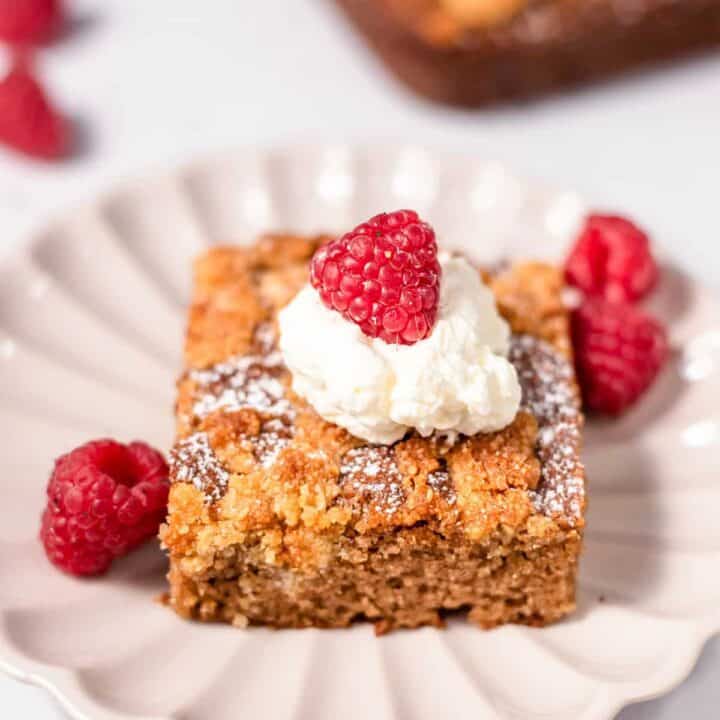 close up of a slice of keto coffee cake topped with whipped cream and a raspberry