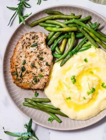 Top view photo of a plate with a Pan Seared Pork Chop, mashed potatoes, and steamed green beans, ready to eat.