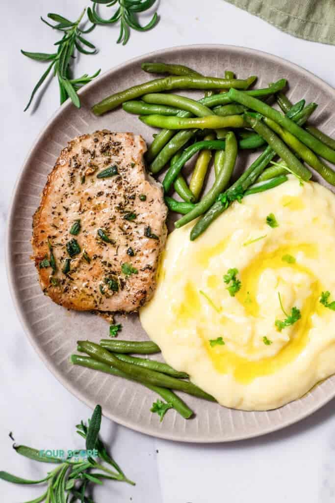 Top view photo of a plate with a Pan Seared Pork Chop, mashed potatoes, and steamed green beans, ready to eat.