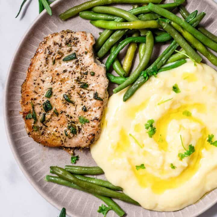 Top view photo of a plate with a Pan Seared Pork Chop, mashed potatoes, and steamed green beans, ready to eat.