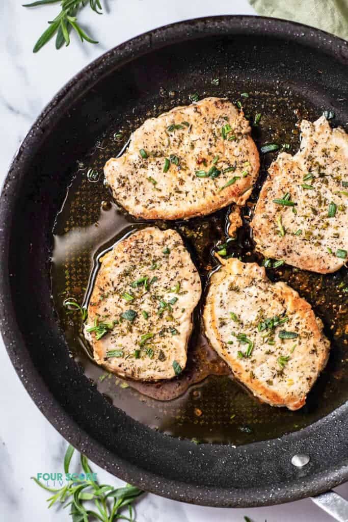 Top view photo of 4 pork chops in a pan, and seared until golden brown.