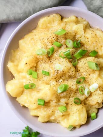 Top view photo of stewed potatoes, garnished with chopped green onions. There is a kitchen towel above the bowl.