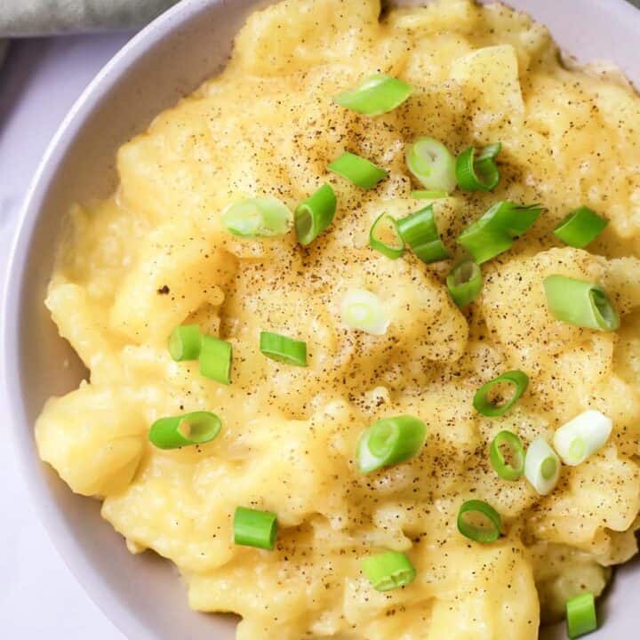 Top view photo of stewed potatoes, garnished with chopped green onions. There is a kitchen towel above the bowl.