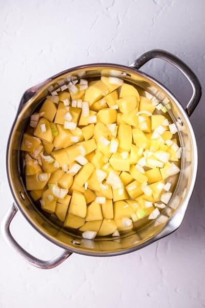 Top view photo of a large stock pot with cubed potatoes and chopped onion and water, ready to boil.