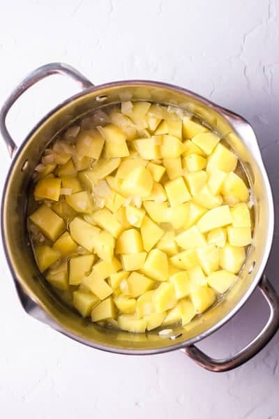 Top view photo of a stock pot with cubed potatoes and water, simmering.