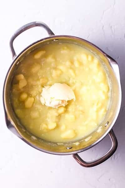 Top view photo of a stock pot with butter, salt, and pepper added to stewed potatoes.