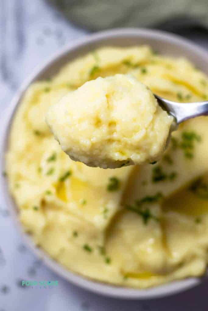 Top view photo of a spoonful of Whipped Potatoes, scooping it up from a bowl of potatoes with melted butter and chives on top.