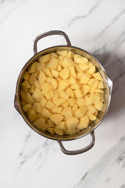Top view photo of a large stockpot filled with chopped potatoes and cold water.