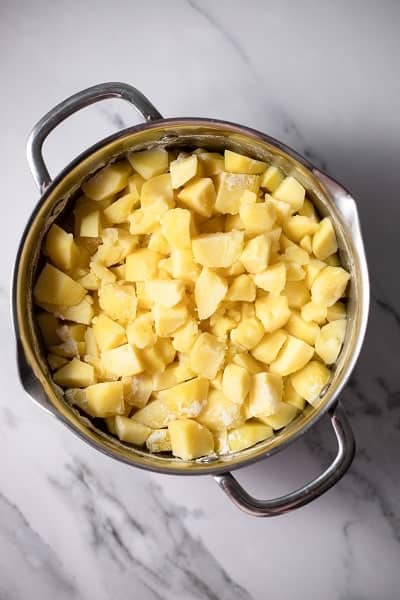 Top view photo of a large stockpot with chopped potatoes and water, and boiling until tender.