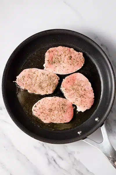 Top view photo of a frying pan with 4 pork chops in the pan.