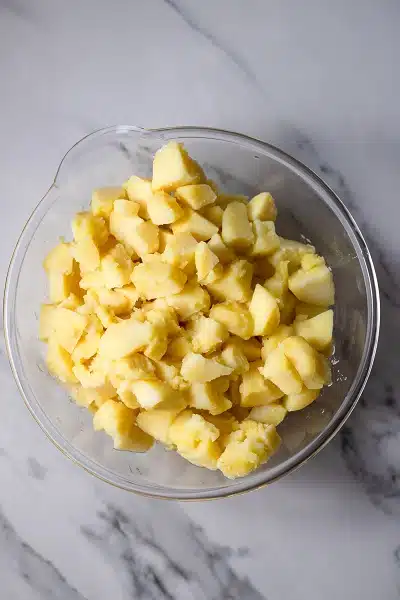 Top view photo of a large clear bowl filled with drained, boiled potatoes.