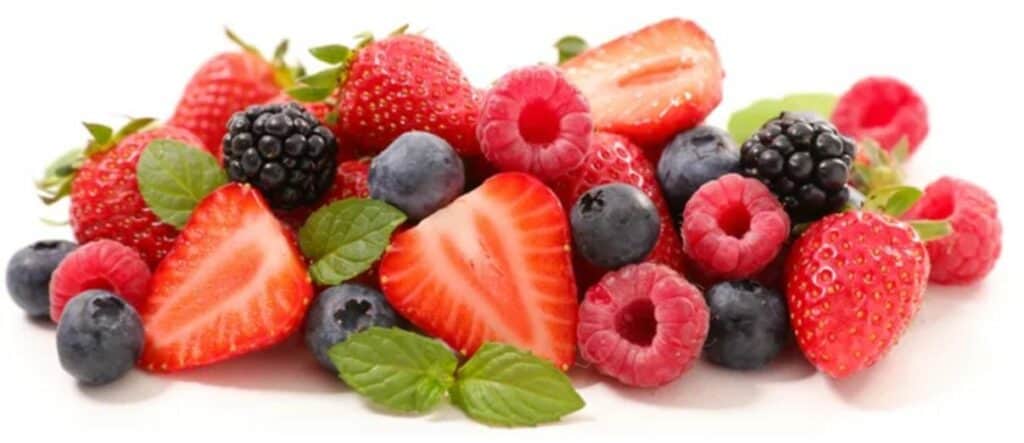 fresh blueberries and raspberries, whole strawberries and sliced strawberries clustered together with green leafy garnish on a white background.