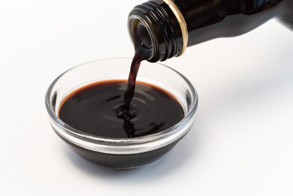 Small glass dish filled with balsamic vinegar and a dark glass bottle of balsamic vinegar pouring into it.
