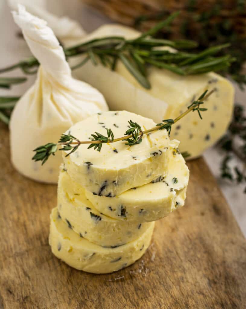 Butter rolled up with herbs in parchment paper. Butter with thyme and rosemary and lemon zest. sliced on and stacked in a tower of 4 of a wooden board.