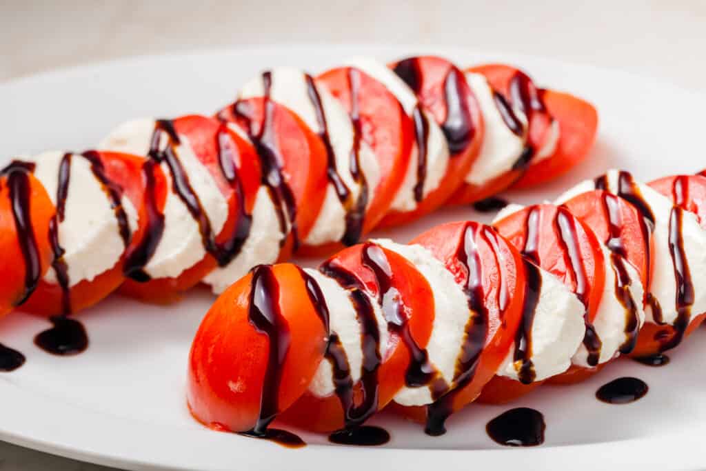 sliced tomatoes layered with fresh slices of mozzarella and balsamic cream on a white platter.