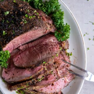 Cooked sirloin tip roast sprinkled with herbs and sliced onto an oval white platter.