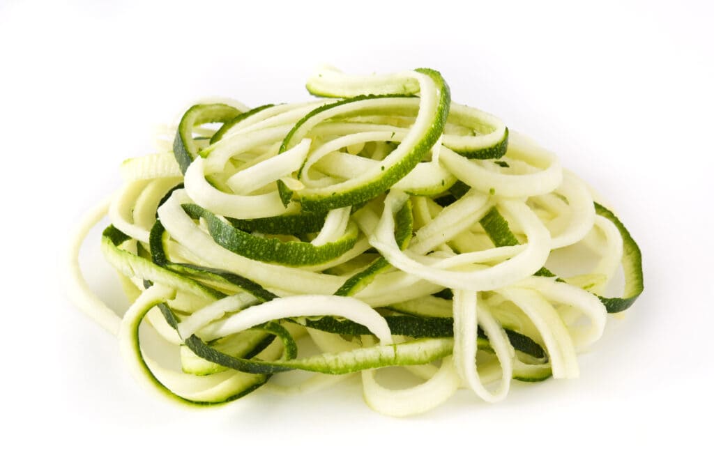 Spiralized fresh zucchini noodles on a white background.