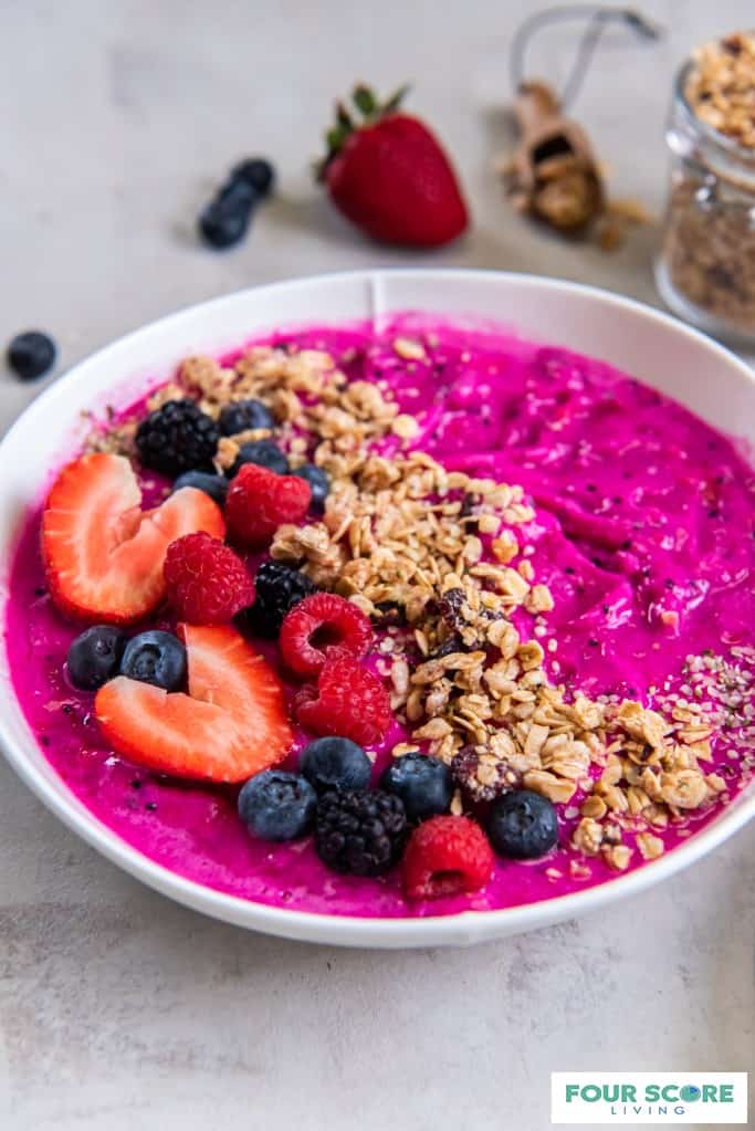 Dragon fruit smoothie  bowl in white bowl with raspberries, blackberries, and sliced strawberries layered on top with granola.