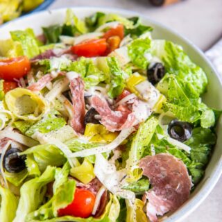 Photo of a large white bowl filled with Grinder Salad. There is a pepper grinder in the background.