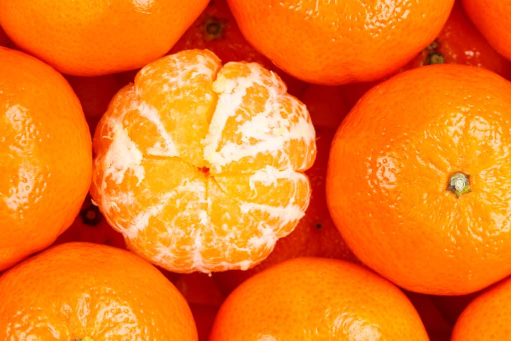 Aerial view of clementine fruits closely packed and stacked in several layers with one clementine in the middle peeled - skin removed. 