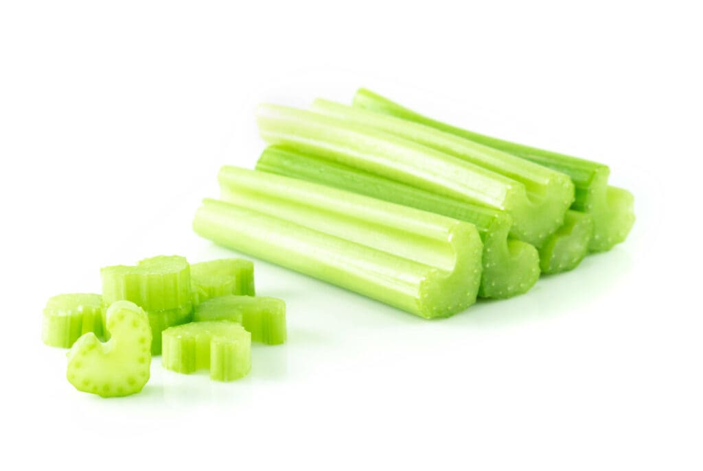 Six fresh celery ribs, each approximately 6 inches in length and ½ inch pices of fresh chopped celery in the foreground, all on a white background.