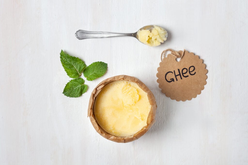 Homemade ghee in a jar, wrapped in parchment paper and an inscription sticker with a green leaf on a white background. Aerial view.