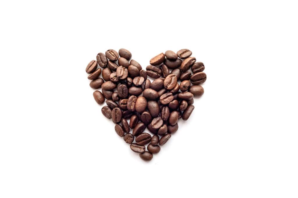 Whole coffee beans in the shape of a heart on a white background.