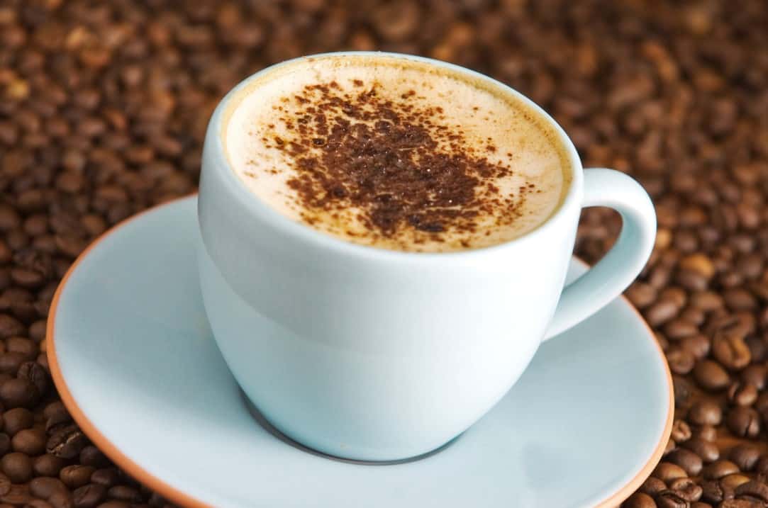 Small white expresso cup and saucer filled with expresso and topped with foam milk and dusted with cocoa powder.