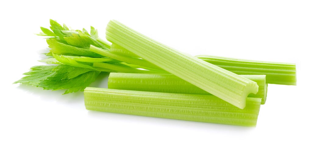 Four celery ribs with a handful of celery leaves on a white background.