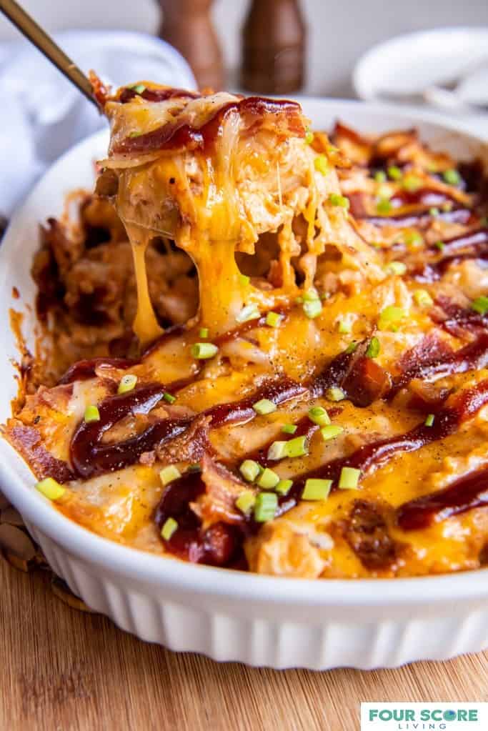 Diagonal up close shot of keto chicken BBQ casserole with a portion being removed with a brass serving utensil and the cheese stretching from the casserole to the utensil. 